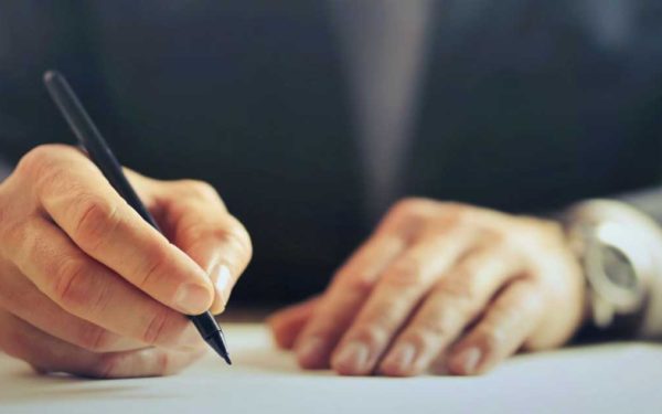 hands-of-a-man-writing-with-pen-sitting-at-desk