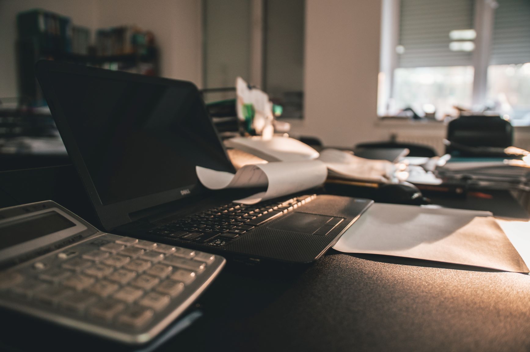laptop-on-desk-with-papers-in-dimly-lit-office