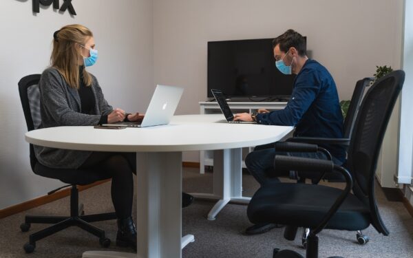 mand-and-woman-sitting-at-conference-table-working-and-wearing-masks