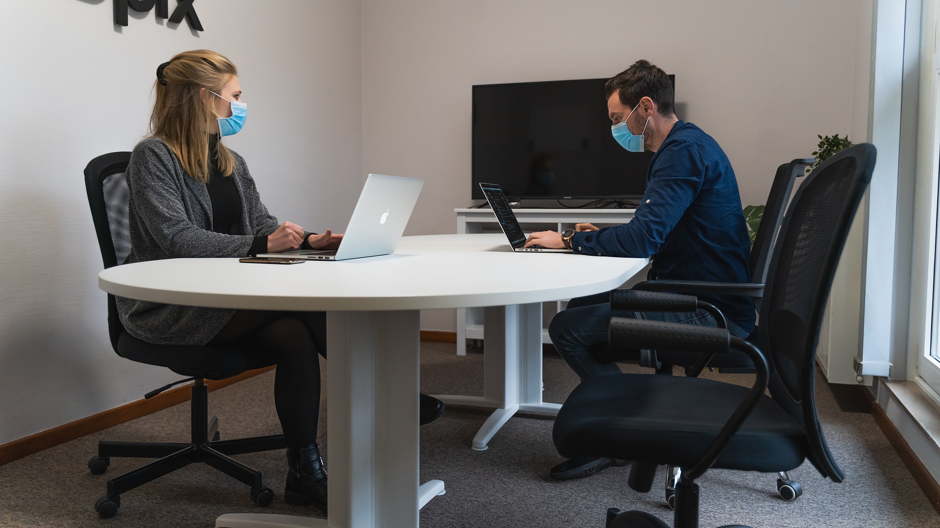 mand-and-woman-sitting-at-conference-table-working-and-wearing-masks