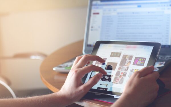 person-scrolling-on-tablet-with-computer-screen-in-background