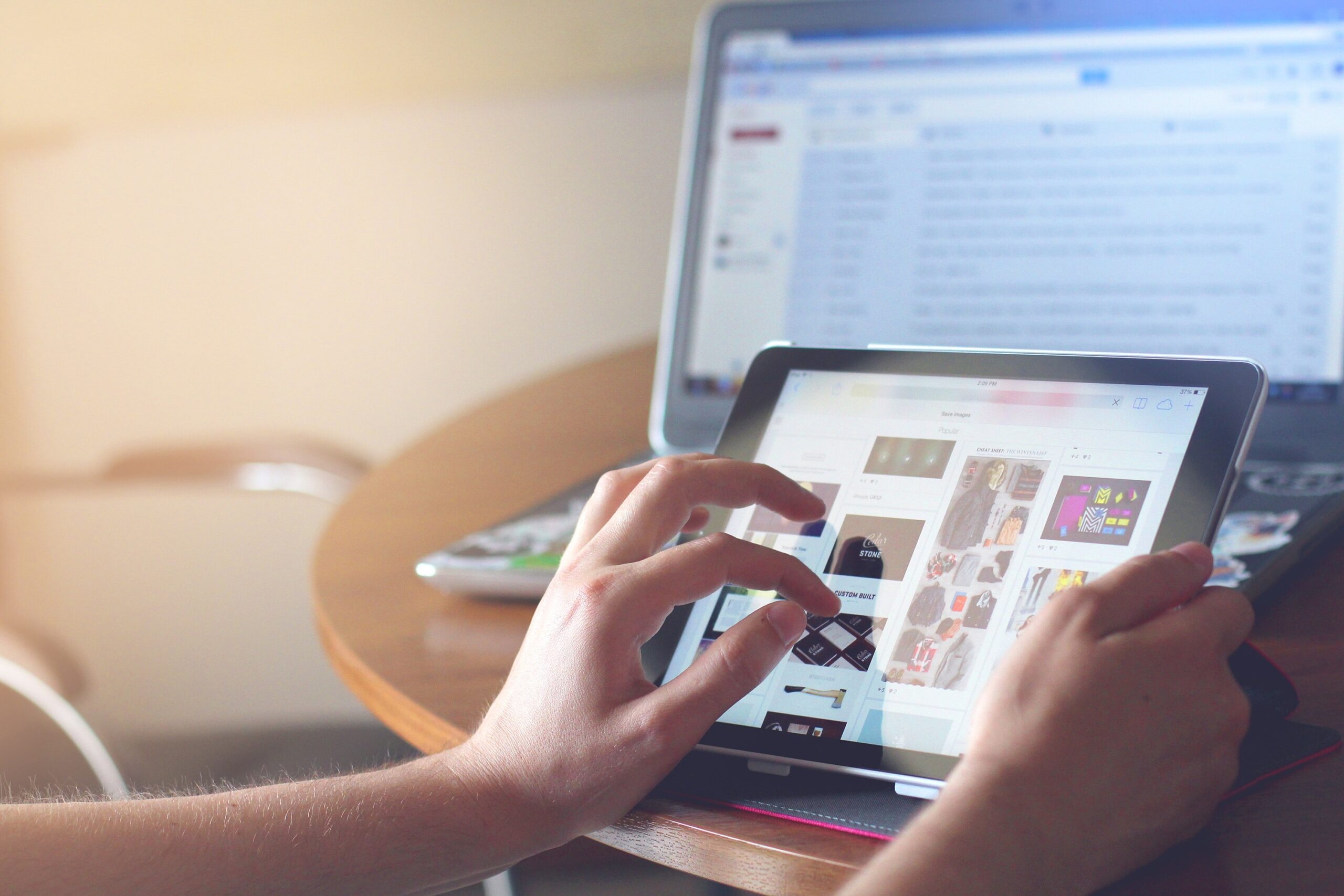 person-scrolling-on-tablet-with-computer-screen-in-background