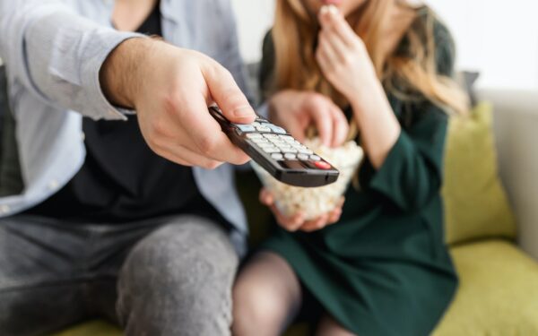 man sitting on couch next to woman holding tv remote and bowl of popcorn