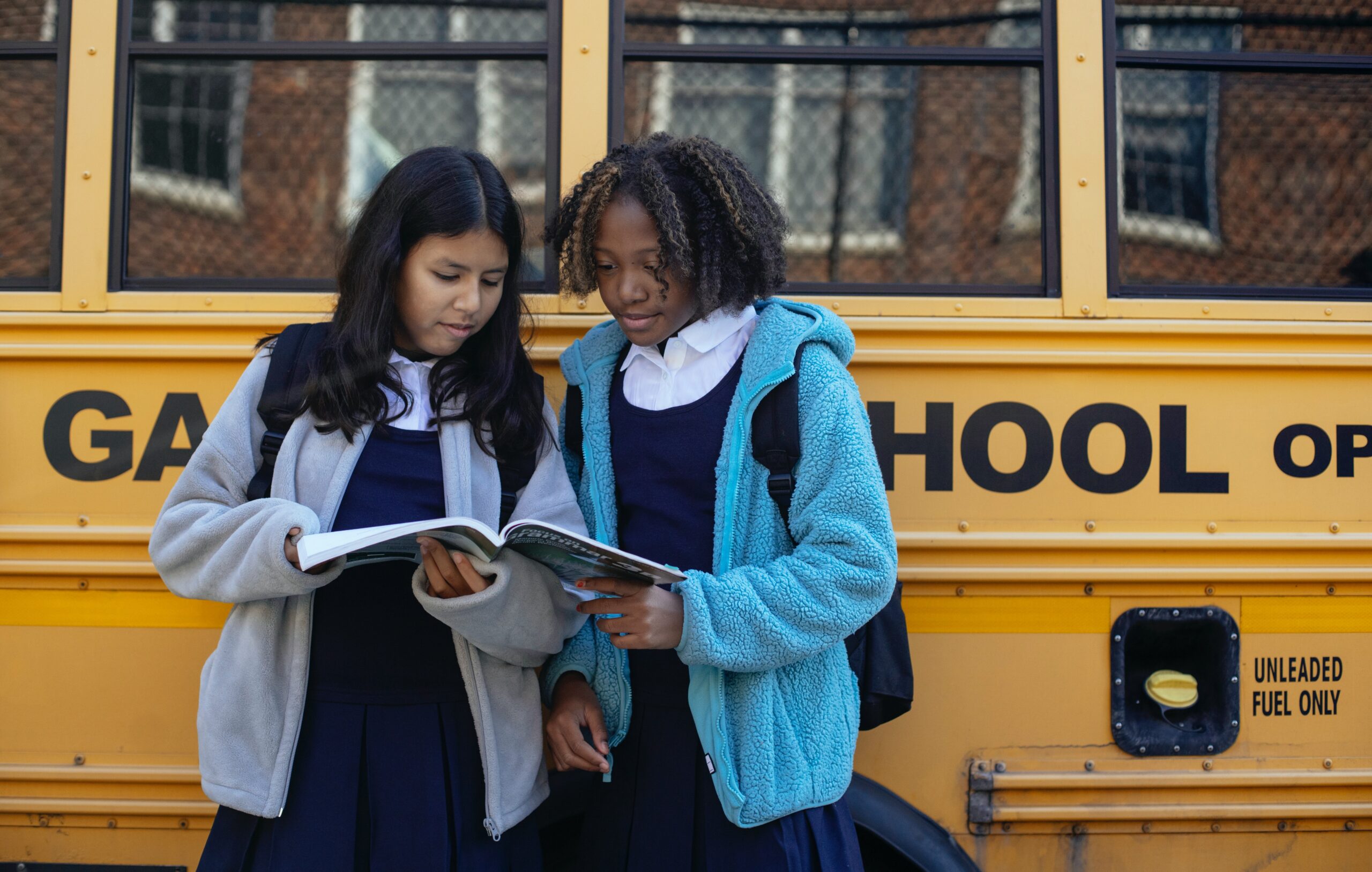 two girls dressed in school uniforms reading a textbook standing up