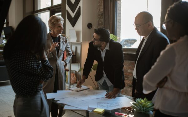 Group of people standing around desk looking at blueprint of office