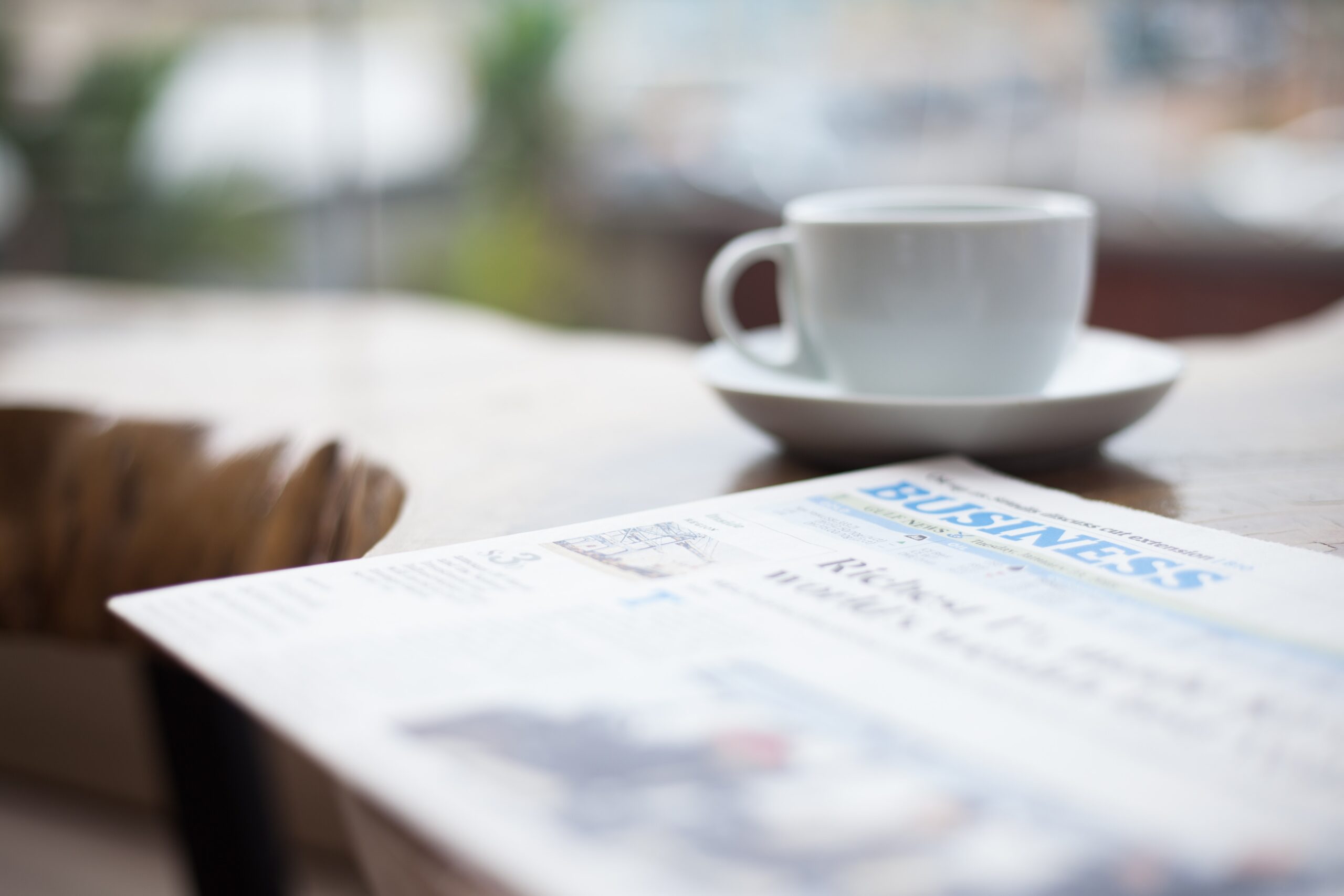 business section of newspaper sitting on desk next to white cup and saucer