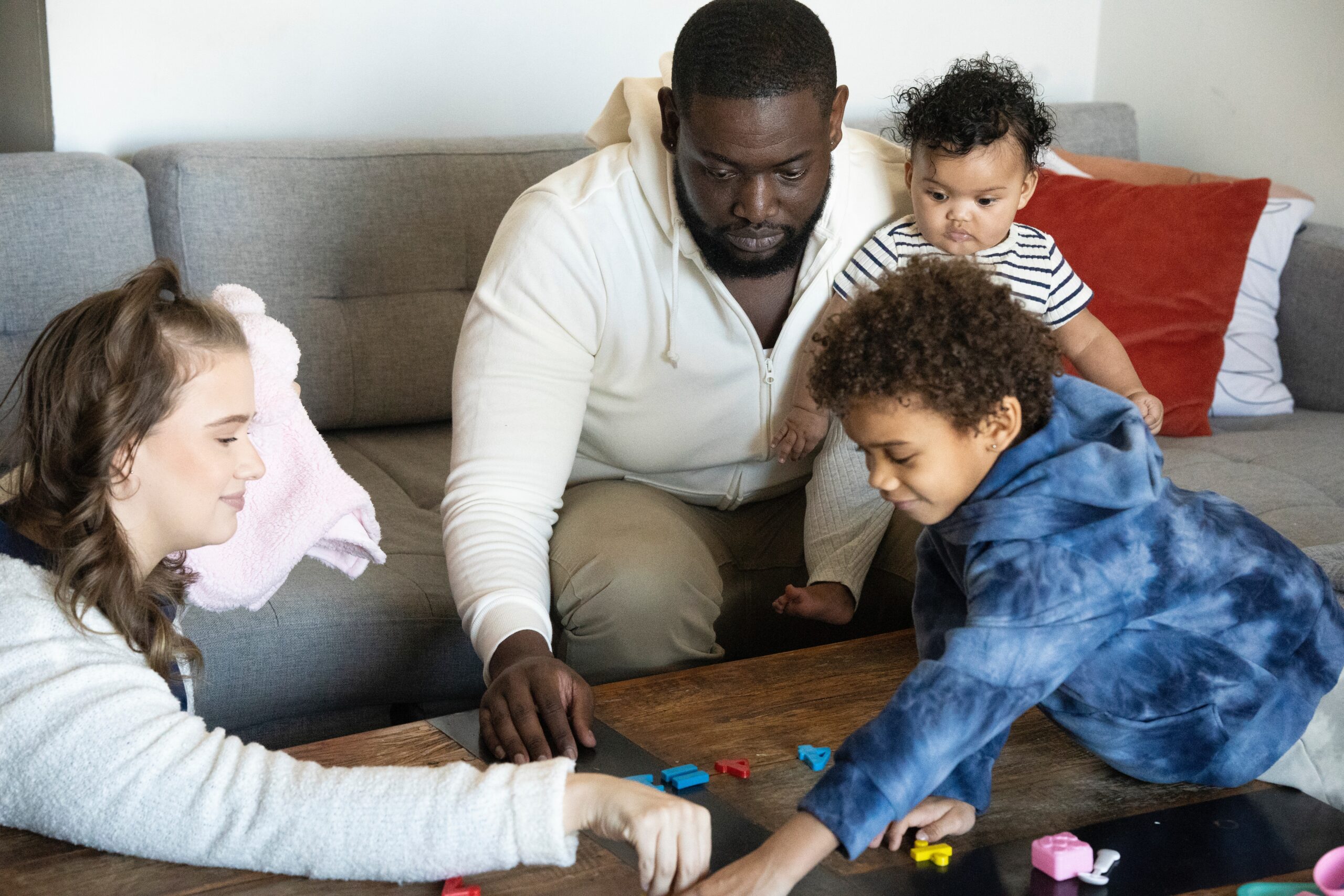 man holding baby while playing with toddler and woman in living room