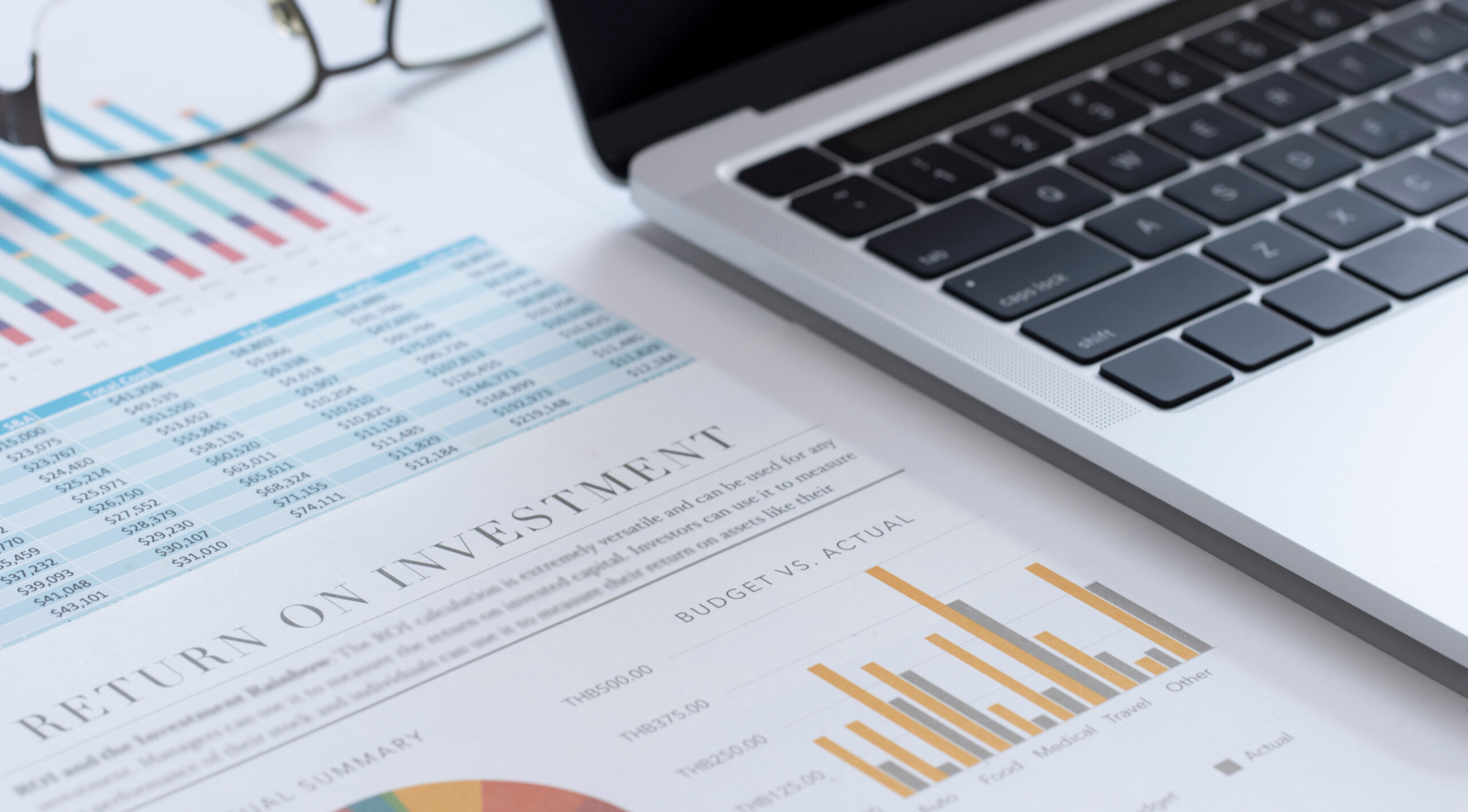 Paper that says Return on investment with data next to open laptop and a pair of reading glasses