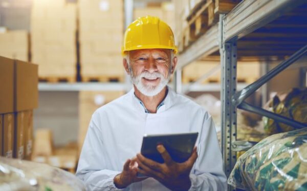 smiling man in yellow helmet holding tablet standing in warehouse