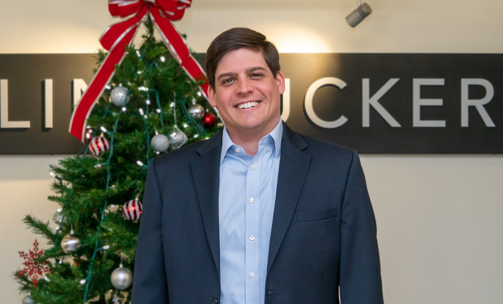 Ellin & Tucker directo Zach Bromwell stands in front of Christmas tree in the Eliin & Tucker lobby