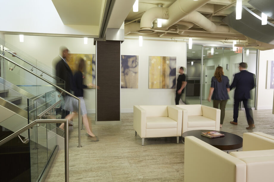 two people walking down the stairs into office lobby while two people walk out the lobby