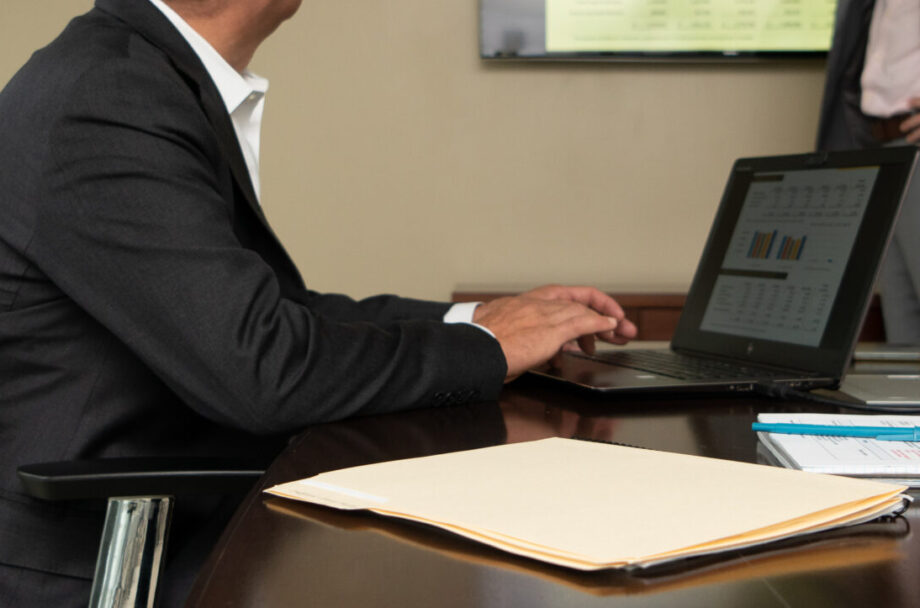 man typing on laptop sitting at conference table
